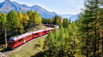 Red train travelling through Alpine mountains