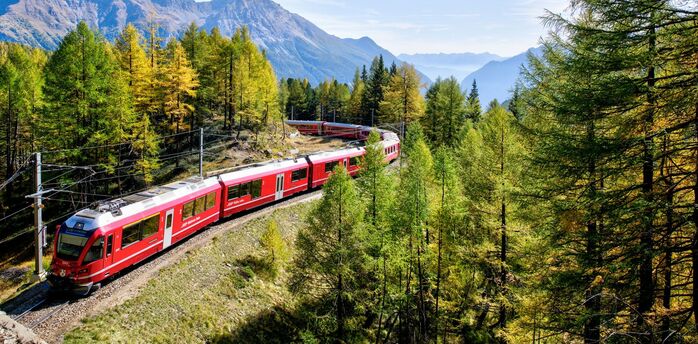 Red train travelling through Alpine mountains