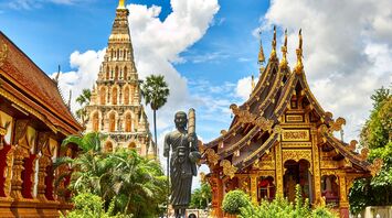Golden Buddhist temple buildings under a bright blue sky in Thailand