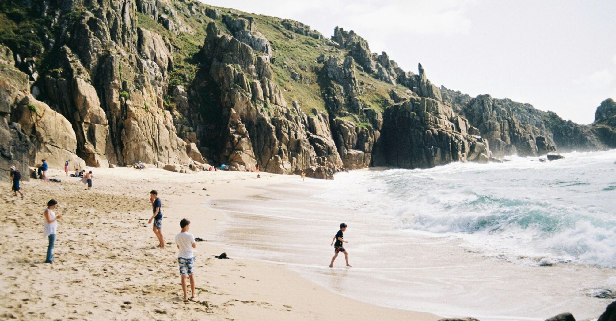 People on a sandy beach below rocky cliffs in Cornwall