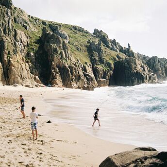 People on a sandy beach below rocky cliffs in Cornwall