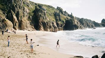 People on a sandy beach below rocky cliffs in Cornwall
