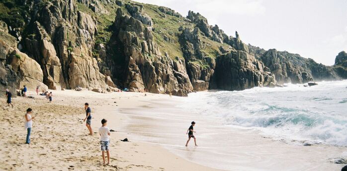 People on a sandy beach below rocky cliffs in Cornwall