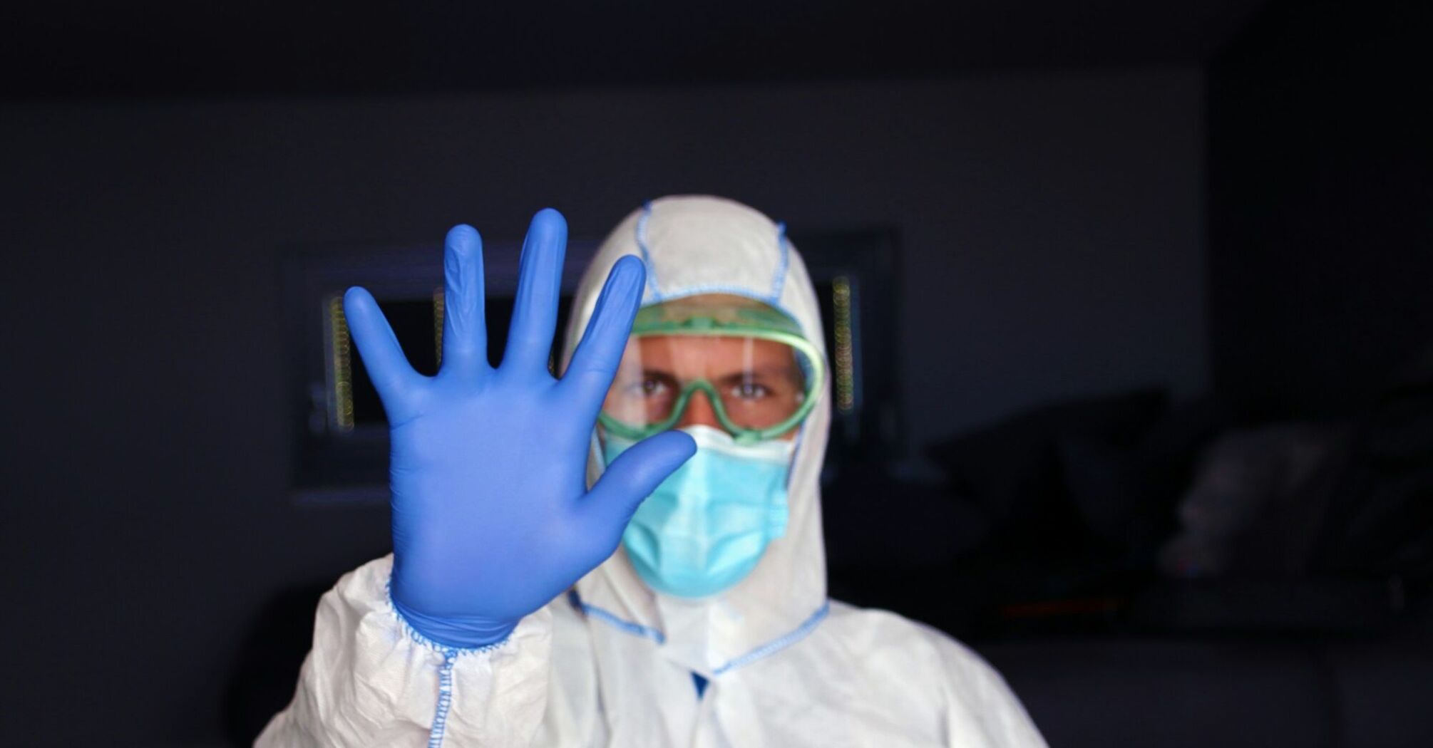 Health worker in protective clothing holding up a gloved hand
