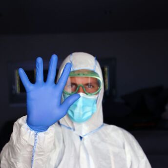 Health worker in protective clothing holding up a gloved hand