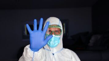 Health worker in protective clothing holding up a gloved hand