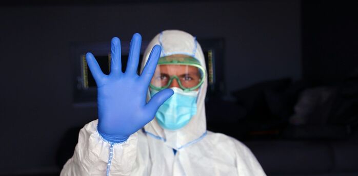 Health worker in protective clothing holding up a gloved hand