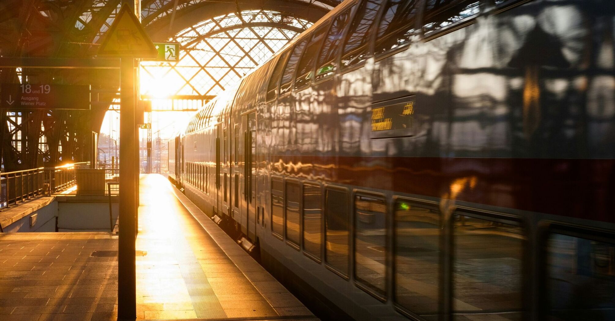 Double-decker train at a railway station during sunset