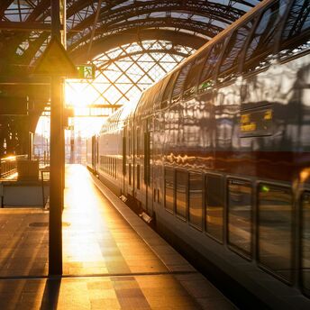 Double-decker train at a railway station during sunset