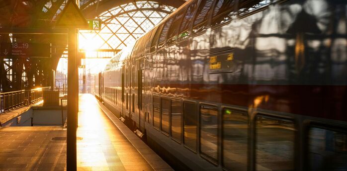 Double-decker train at a railway station during sunset