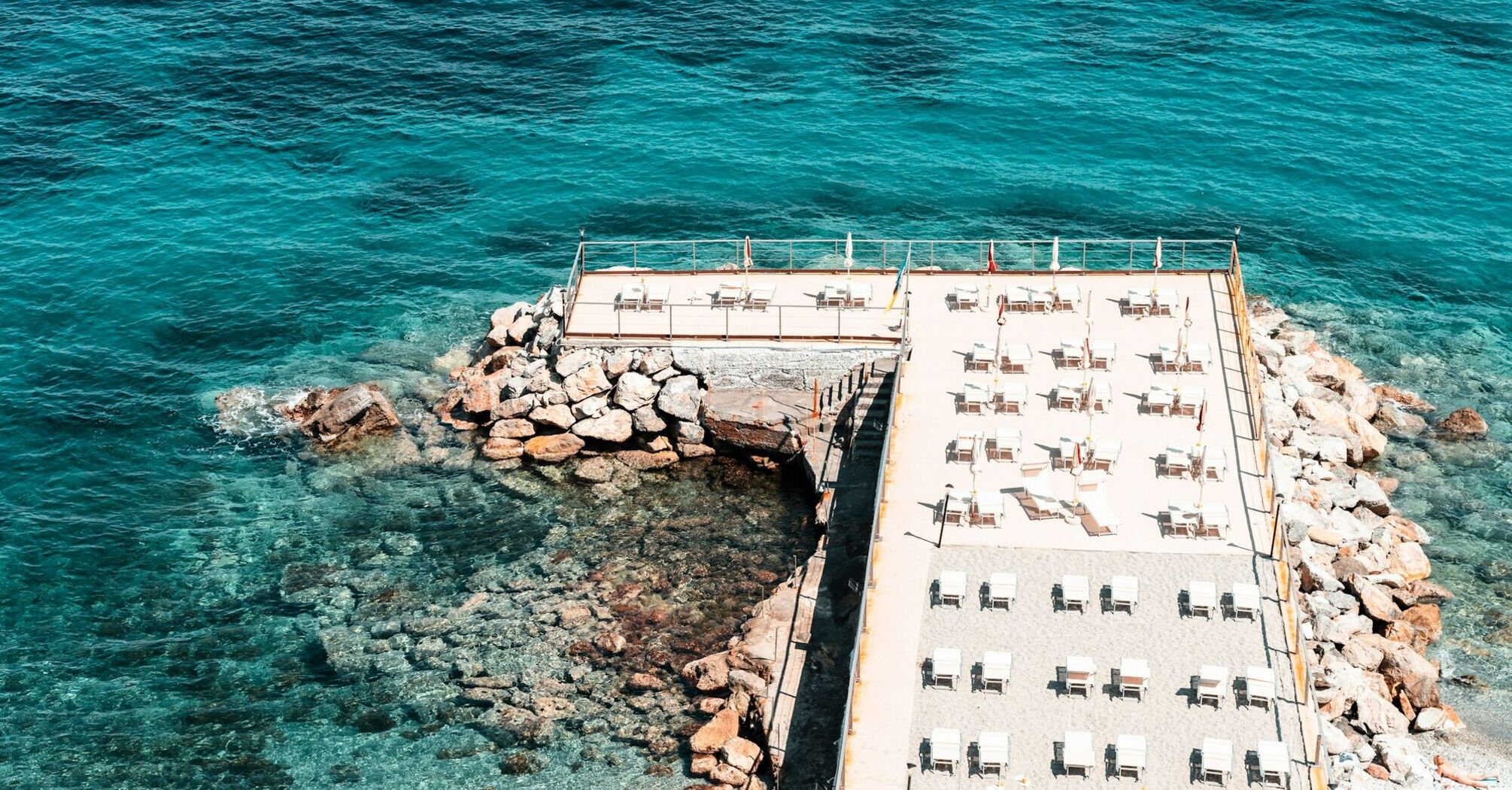 Sun loungers lined up beside clear blue sea