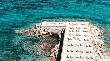 Sun loungers lined up beside clear blue sea