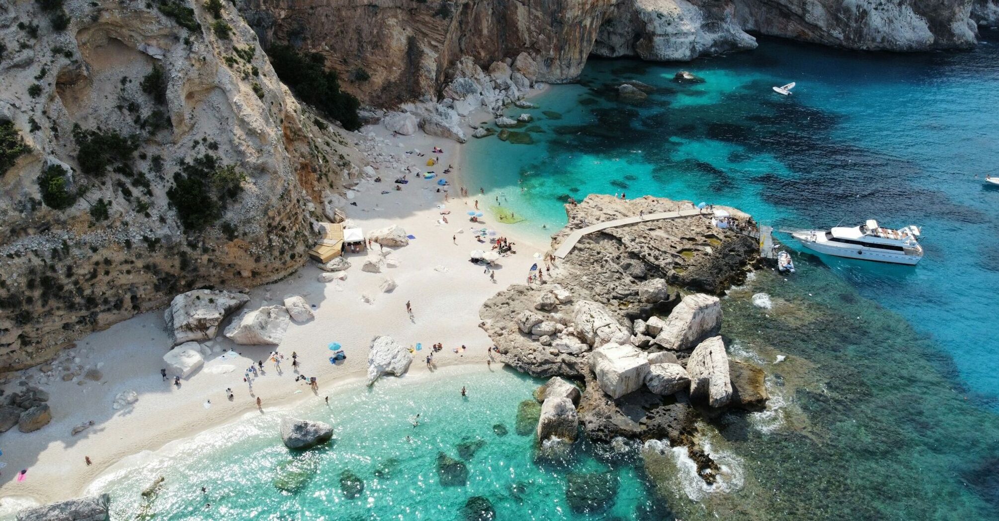 Aerial view of a small Sardinian beach with cliffs, turquoise water and boats