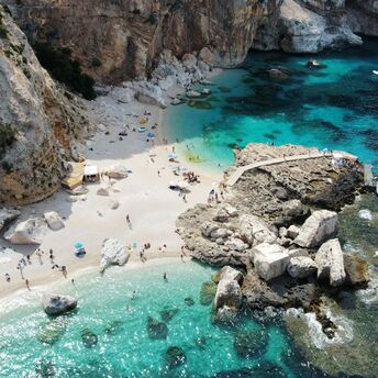 Aerial view of a small Sardinian beach with cliffs, turquoise water and boats