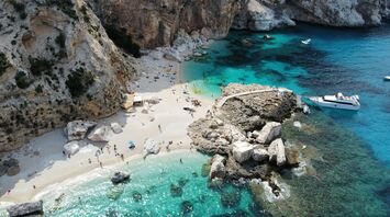 Aerial view of a small Sardinian beach with cliffs, turquoise water and boats