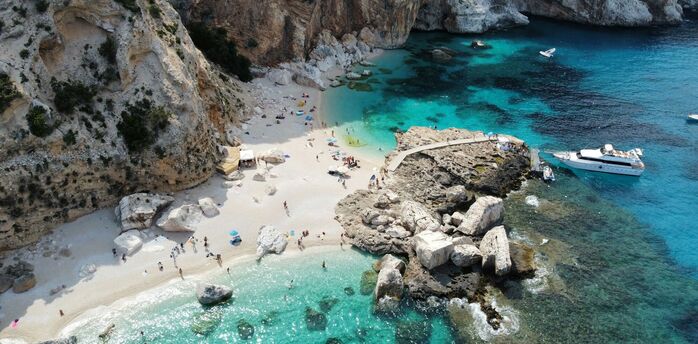 Aerial view of a small Sardinian beach with cliffs, turquoise water and boats