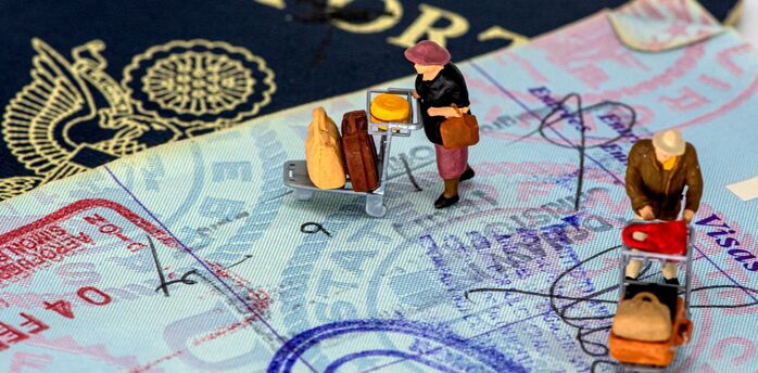 Small traveller figures standing on passport pages with visa stamps
