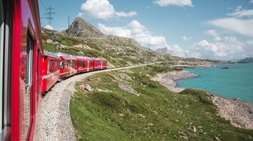 Red train passing a mountain lake
