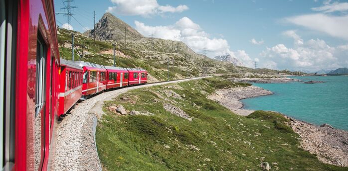 Red train passing a mountain lake