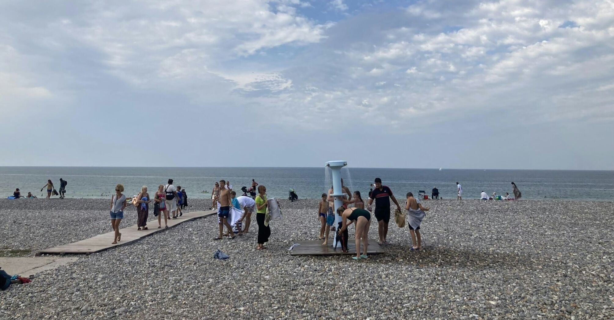 Beachgoers using a shower on a pebbled beach