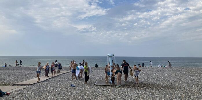 Beachgoers using a shower on a pebbled beach