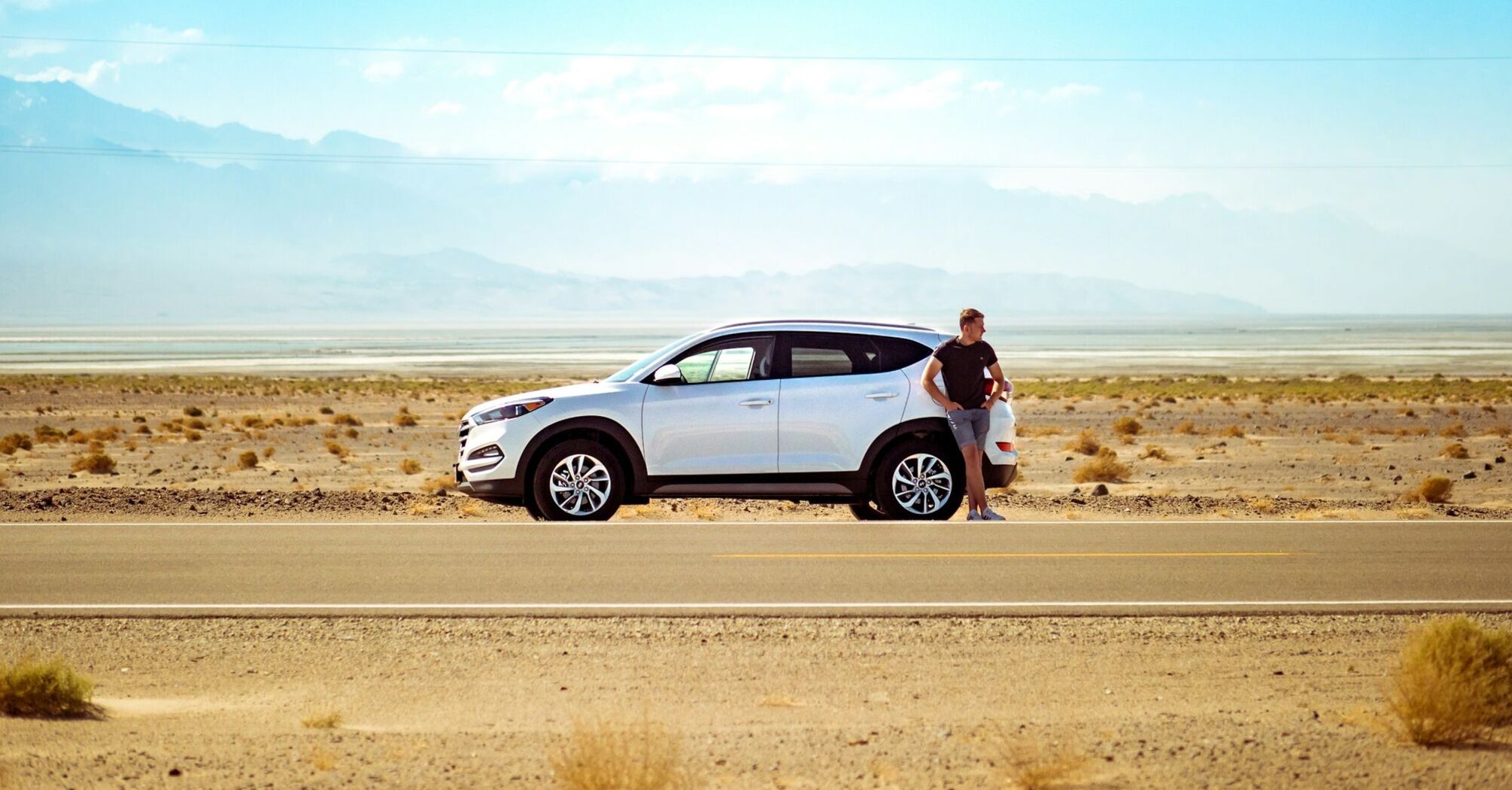 Driver standing beside a rental car on a road
