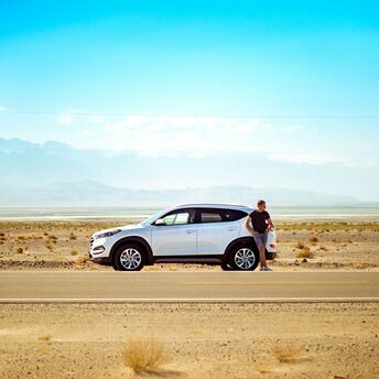 Driver standing beside a rental car on a road