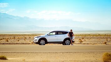 Driver standing beside a rental car on a road