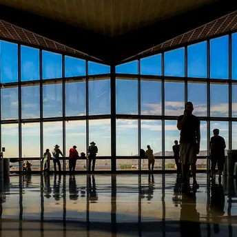 Passengers waiting inside an airport terminal near large windows