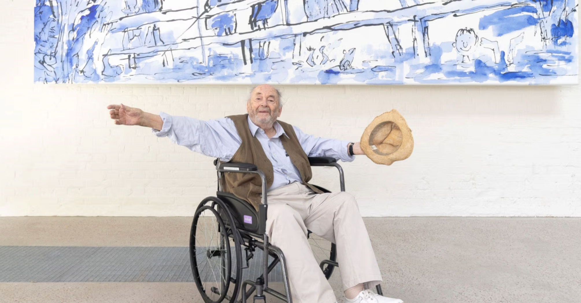 Quentin Blake sitting in a wheelchair below a large blue illustration