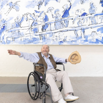 Quentin Blake sitting in a wheelchair below a large blue illustration