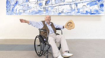 Quentin Blake sitting in a wheelchair below a large blue illustration