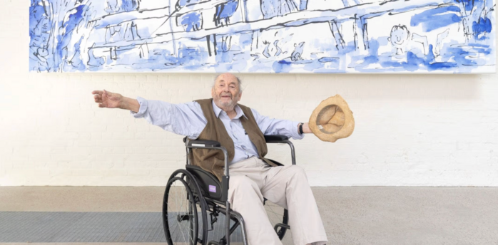 Quentin Blake sitting in a wheelchair below a large blue illustration