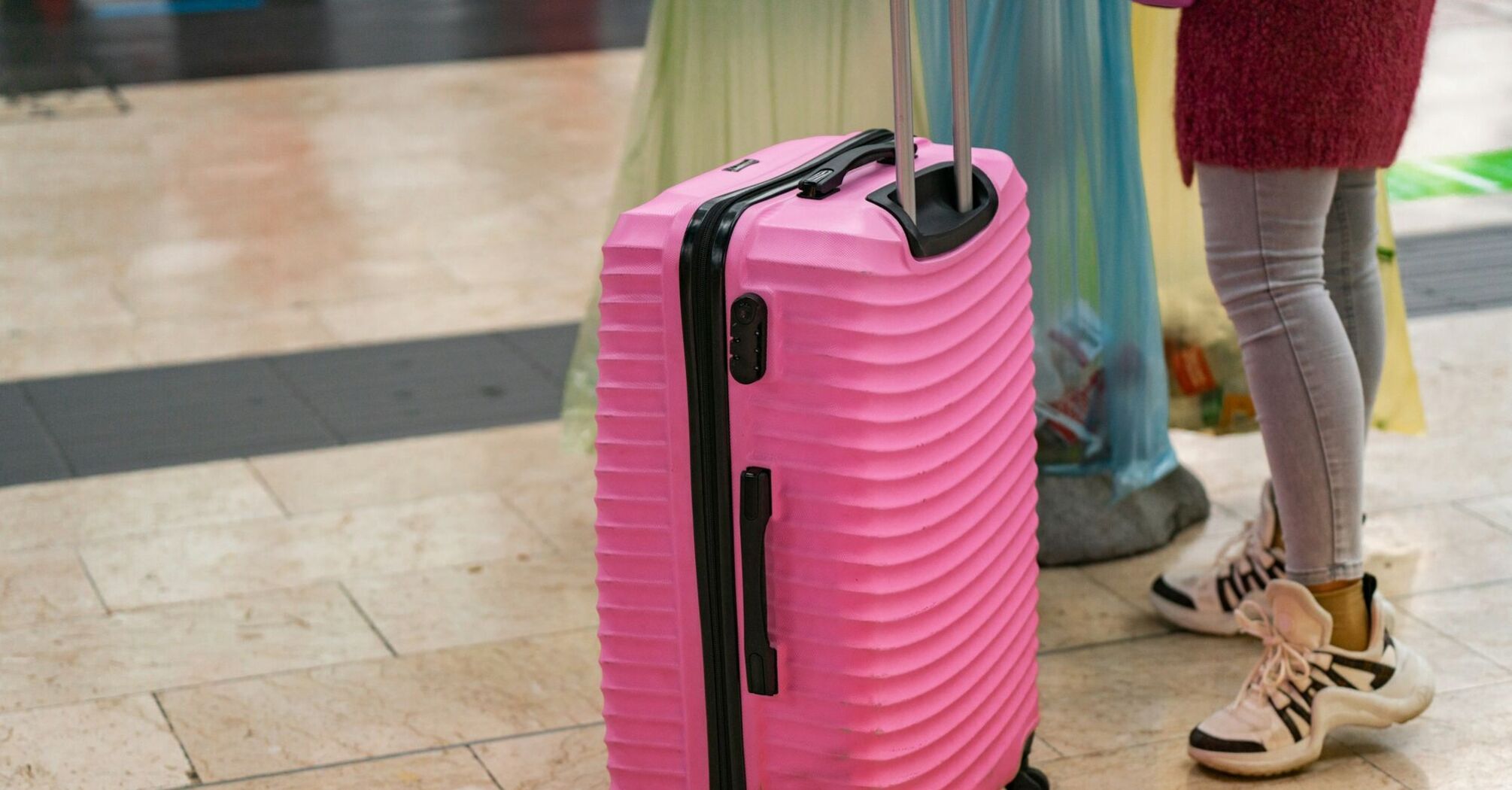 Pink suitcase standing on an airport floor beside a passenger