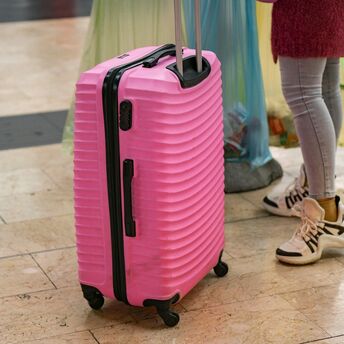 Pink suitcase standing on an airport floor beside a passenger