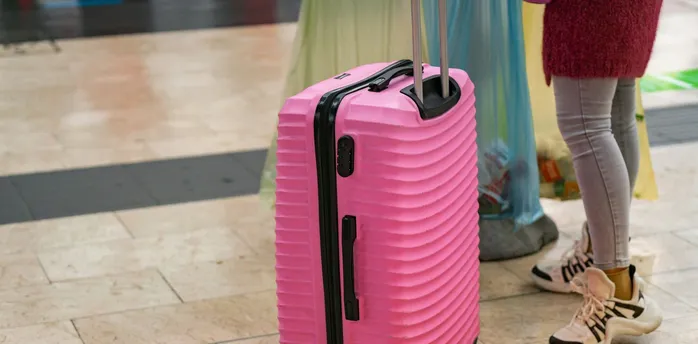 Pink suitcase standing on an airport floor beside a passenger