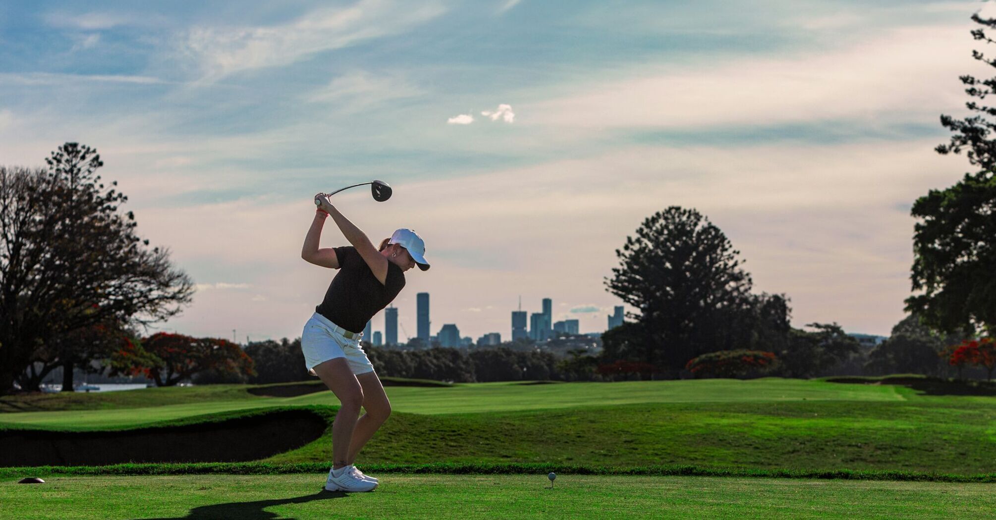 Golfer taking a tee shot with a city skyline behind