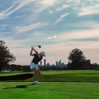 Golfer taking a tee shot with a city skyline behind