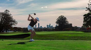 Golfer taking a tee shot with a city skyline behind