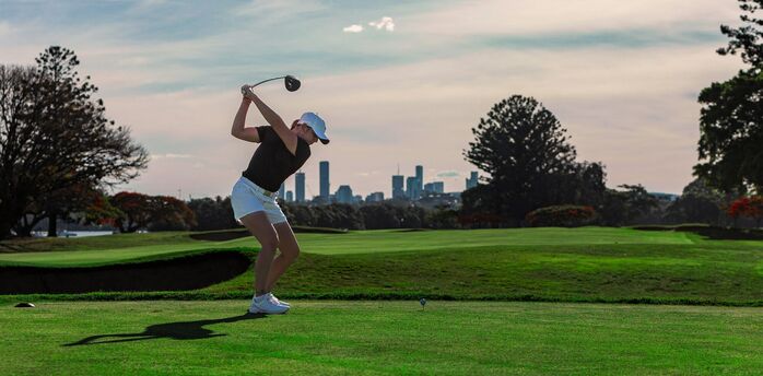 Golfer taking a tee shot with a city skyline behind