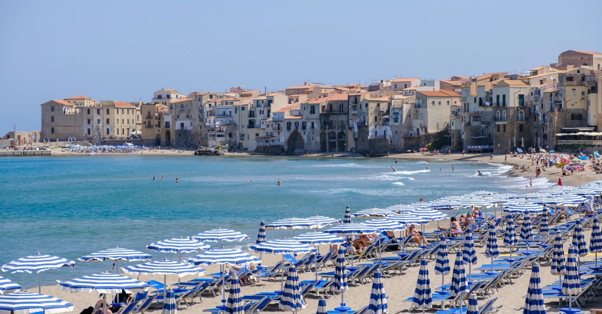 Cefalù beach with striped umbrellas and historic seaside town in Italy