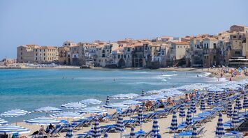 Cefalù beach with striped umbrellas and historic seaside town in Italy