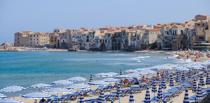 Cefalù beach with striped umbrellas and historic seaside town in Italy
