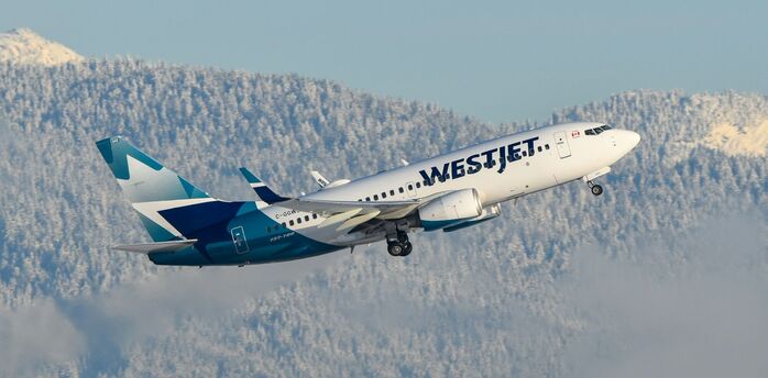 WestJet aircraft flying over snowy mountains