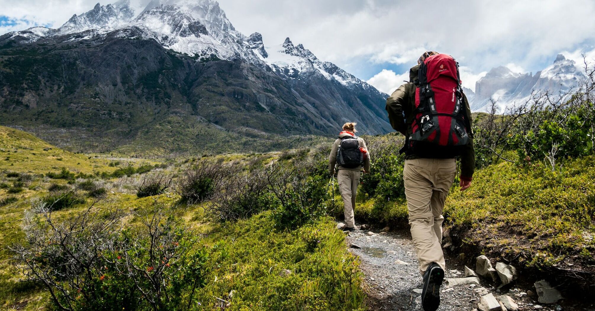 Two hikers walking towards snowy mountains