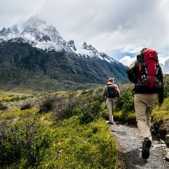 Two hikers walking towards snowy mountains
