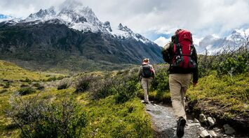 Two hikers walking towards snowy mountains