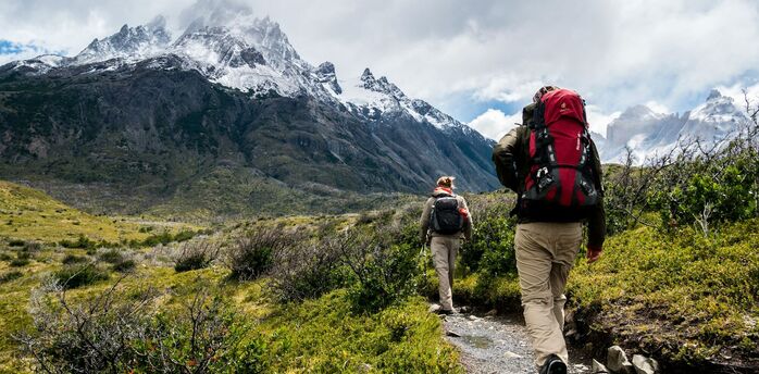 Two hikers walking towards snowy mountains