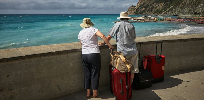 Older couple travelling with luggage by the sea