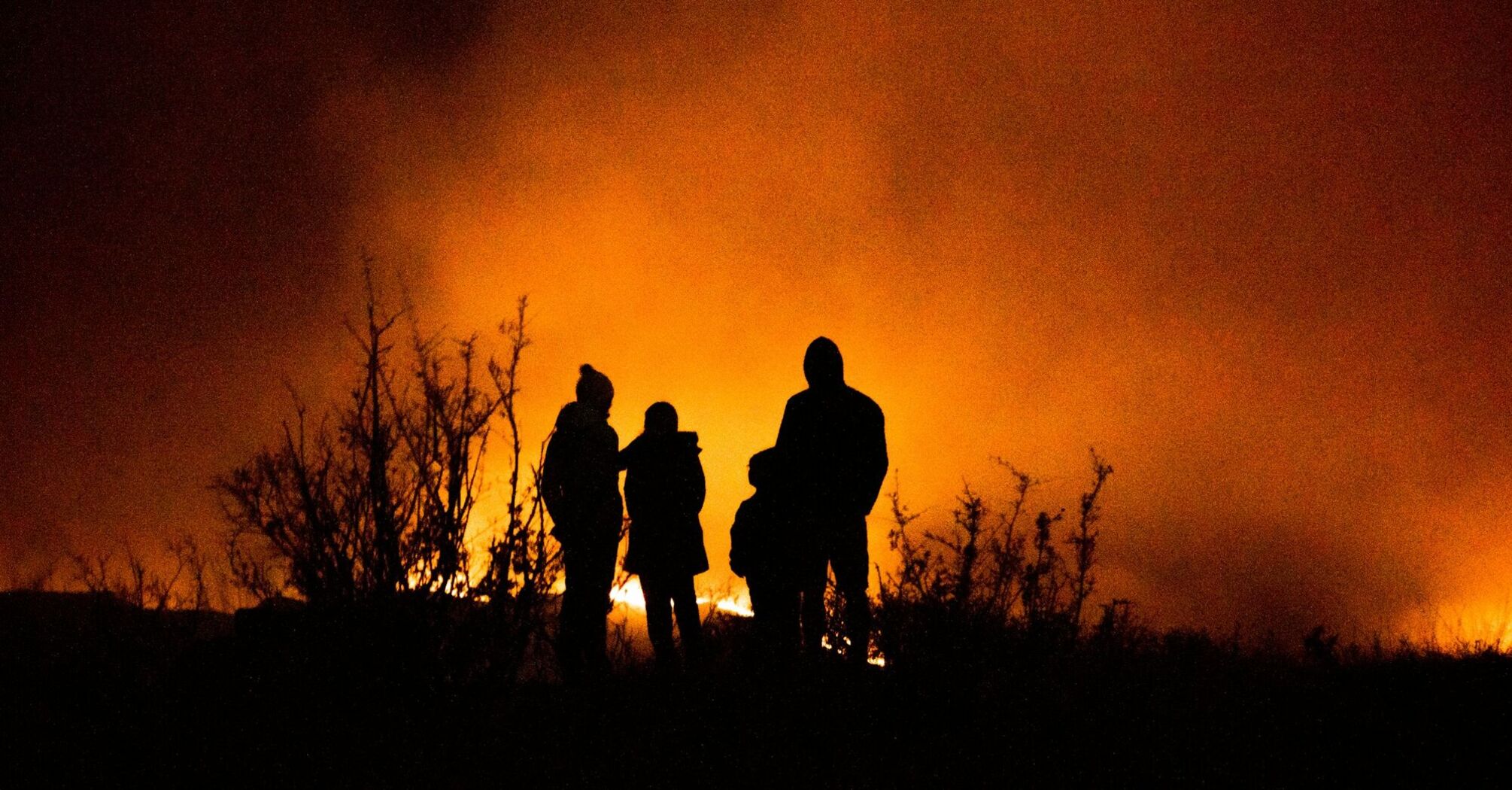 People standing near a large wildfire at night
